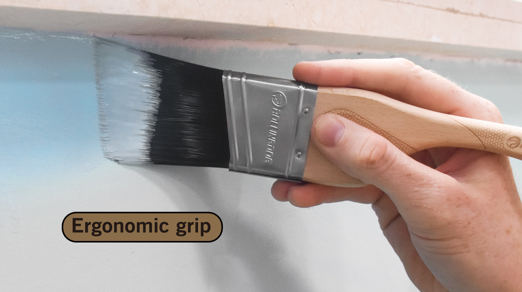 Hand holding a paintbrush with ergonomic grip on a white wall background