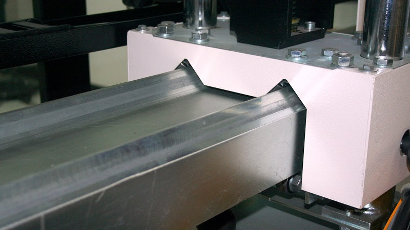 Close-up of a metalworking machine with a conveyor belt and mechanical components.