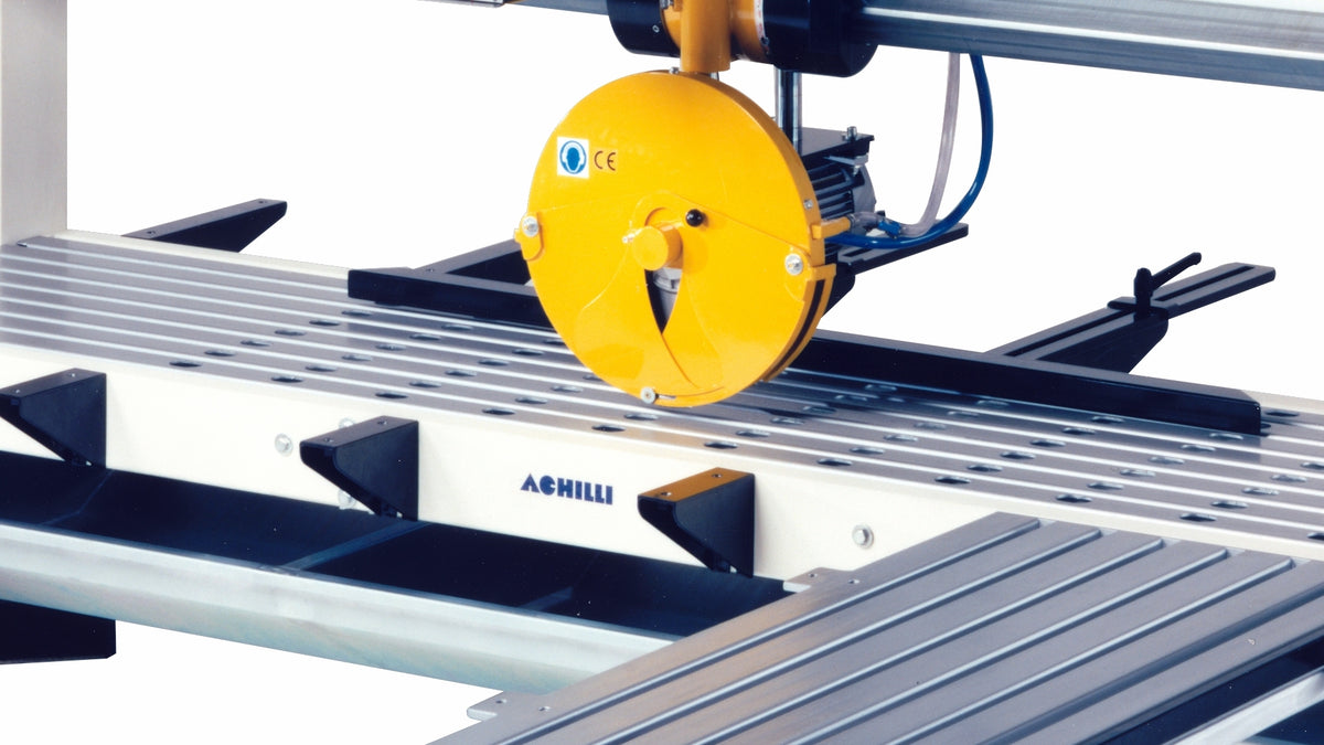 A close-up of an industrial table saw guide system featuring a bright yellow circular safety guard, black metal rails, and a white guide rail with the brand name 'ACHILLI' printed on it.